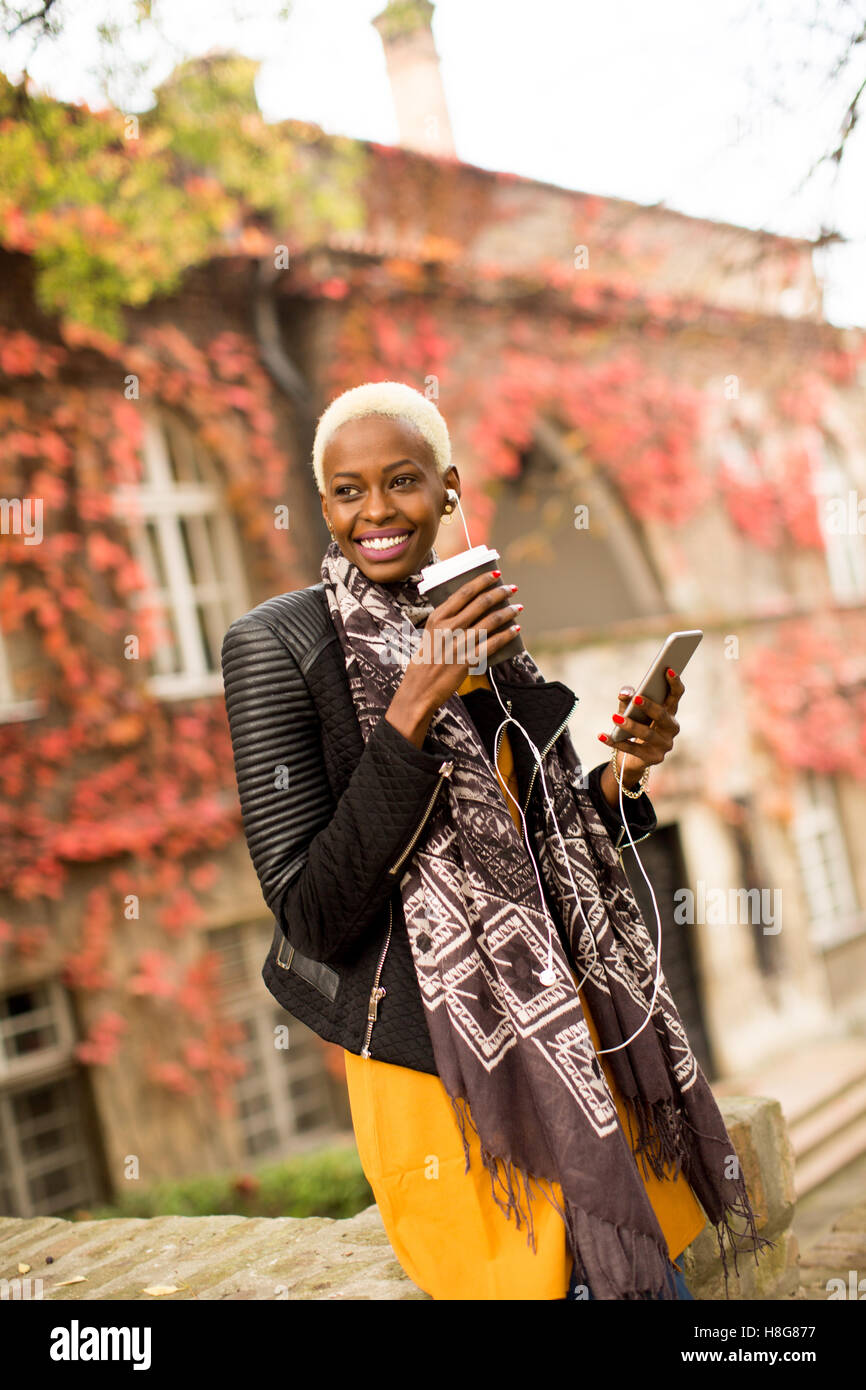 Moderno e giovane africano donna americana in posa con caffè di andare e il telefono cellulare all'aperto Foto Stock
