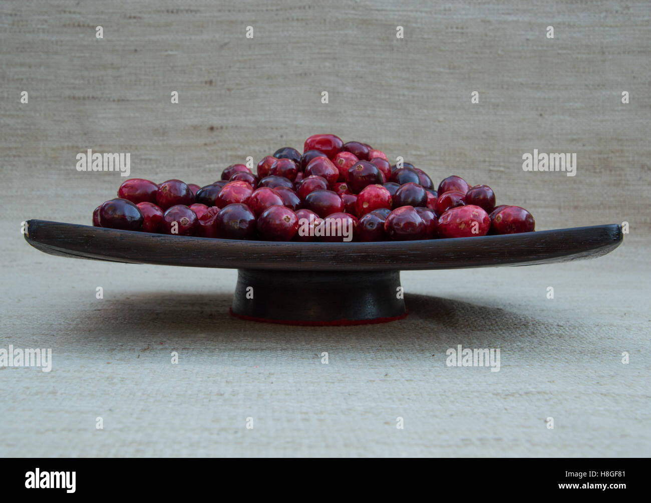 Rosso fresco e maroon cranberries ammucchiò al buio su un tagliere di legno. Fotografato dal di sopra con il flash fill, profondità di campo. Foto Stock
