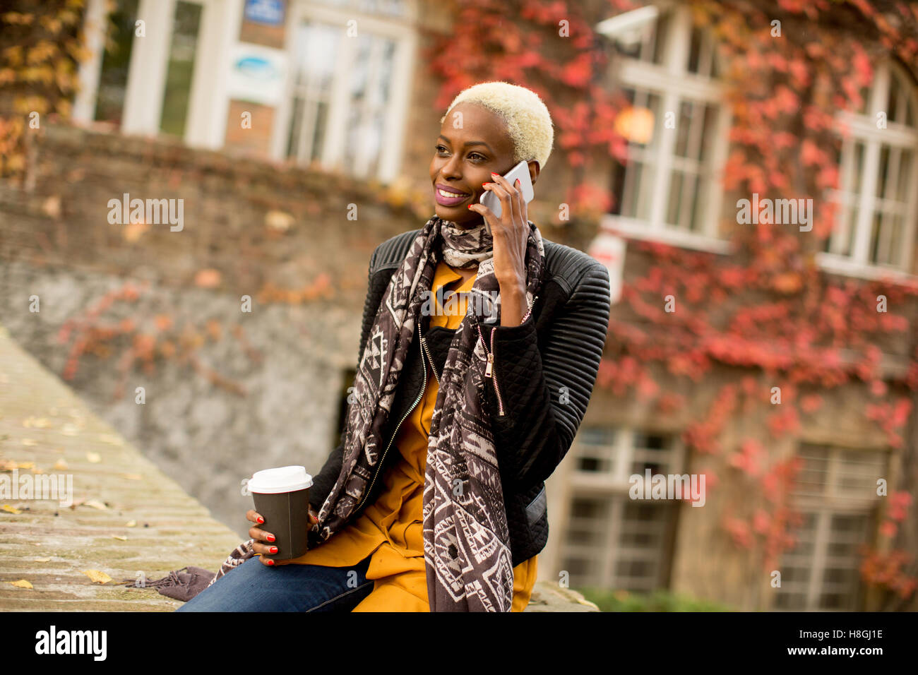 Moderno e giovane africano donna americana in posa con caffè di andare e il telefono cellulare all'aperto Foto Stock