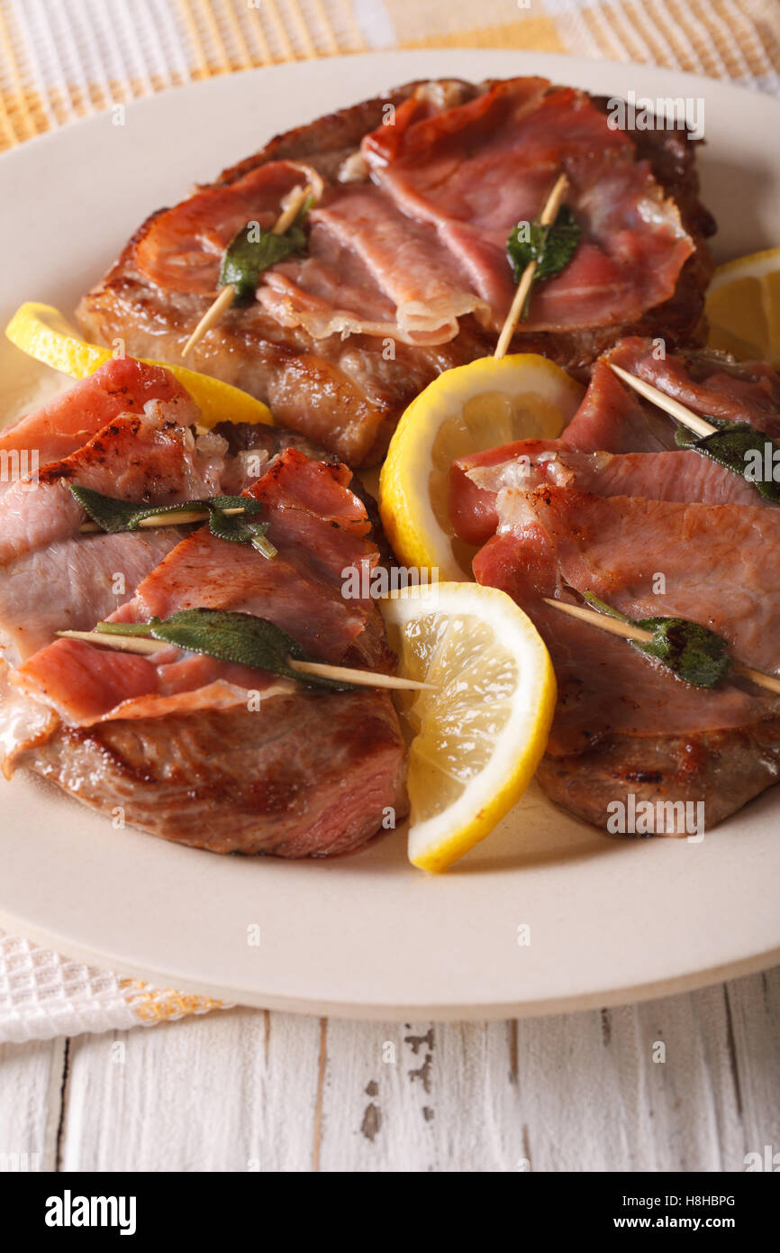 Carne bovina italiana Saltimbocca alla salvia, prosciutto e limone close-up su una piastra. In verticale Foto Stock