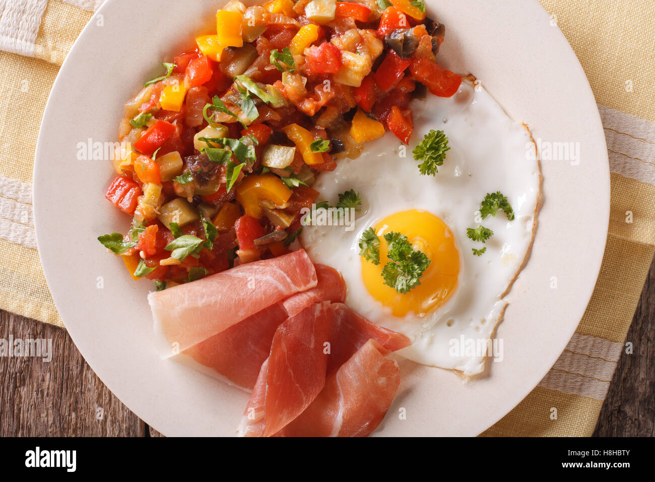 Prima colazione spagnola: uovo fritto, prosciutto e pisto su una piastra sul tavolo. Vista orizzontale dal di sopra Foto Stock