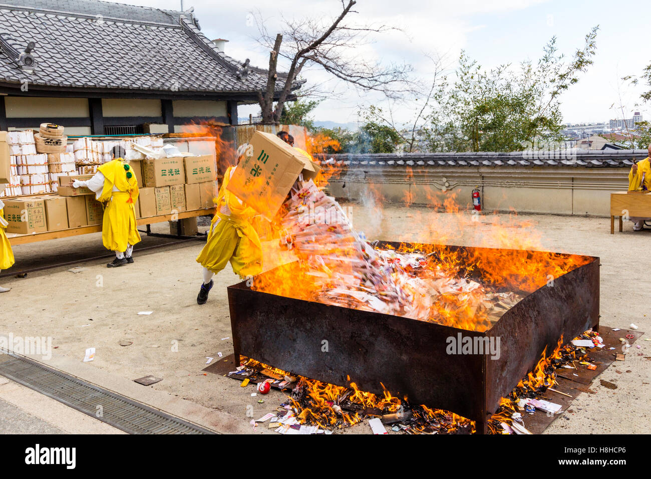 Giappone, Nishinomiya, Mondo Yakujin Tempio. Yamabushi sacerdote in vesti giallo gettando box-carico di gomaki e omikuji, carte e scorre nel fuoco. Foto Stock