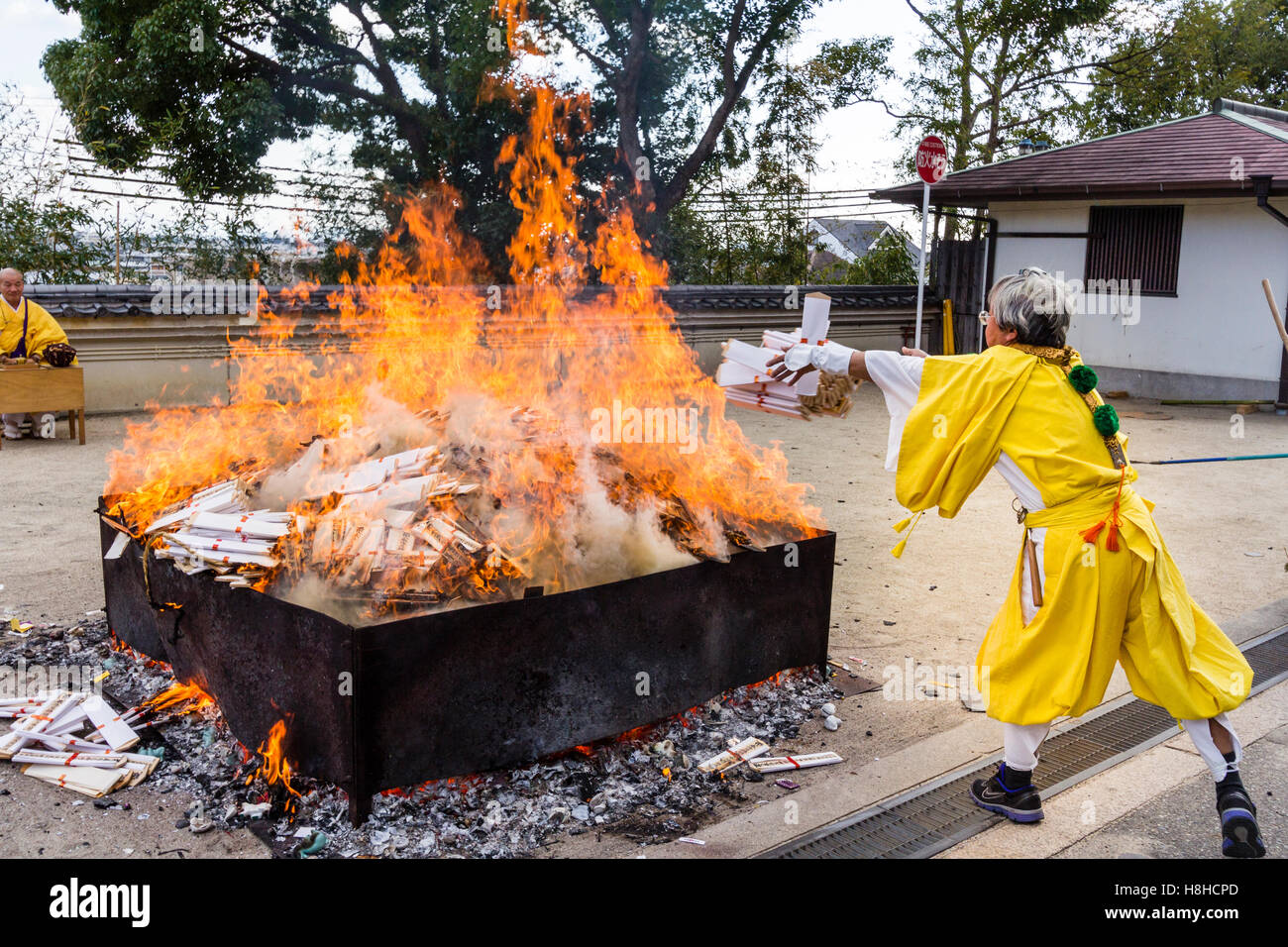 Giappone, Nishinomiya, Mondo Yakujin Tempio. Sacerdote Yamabushi in giallo accappatoi, gettando manciate di gomaki e omikuji, carte e scorre nel fuoco. Foto Stock