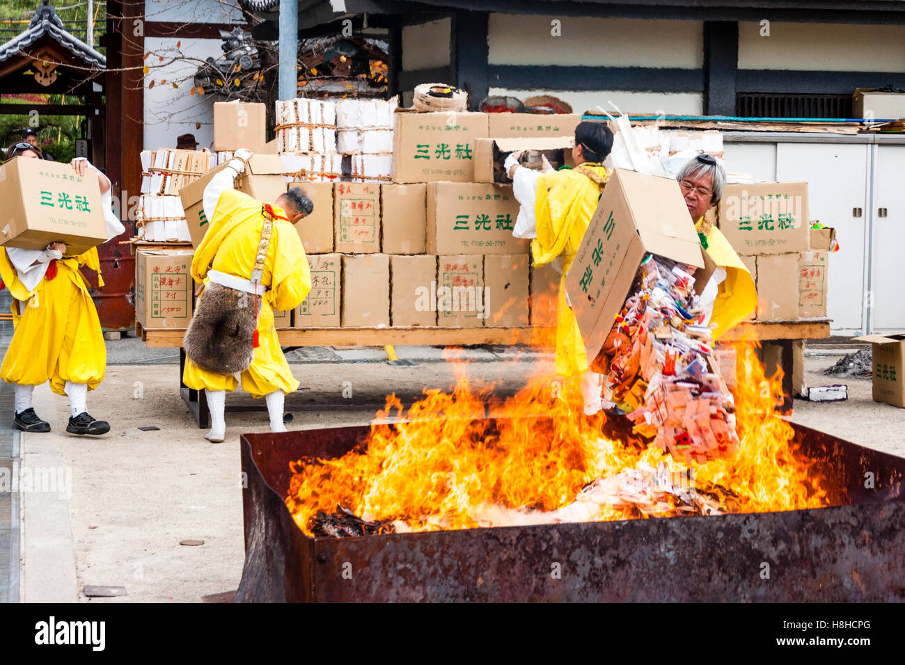 Giappone, Nishinomiya, Mondo Yakujin Tempio. Yamabushi sacerdote in vesti giallo gettando box-carico di gomaki e omikuji, carte e scorre nel fuoco. Foto Stock