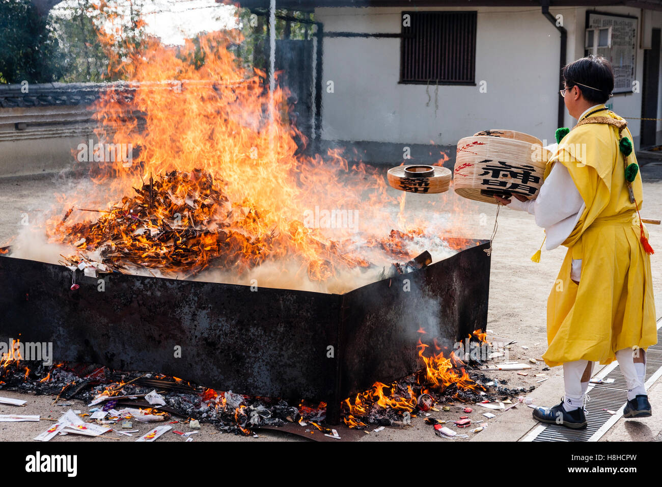 Giappone, Nishinomiya, Mondo Yakujin Tempio. Yamabushi sacerdote in vesti giallo gettando il Bambù Bocce nel fuoco durante la cerimonia di purificazione. Foto Stock