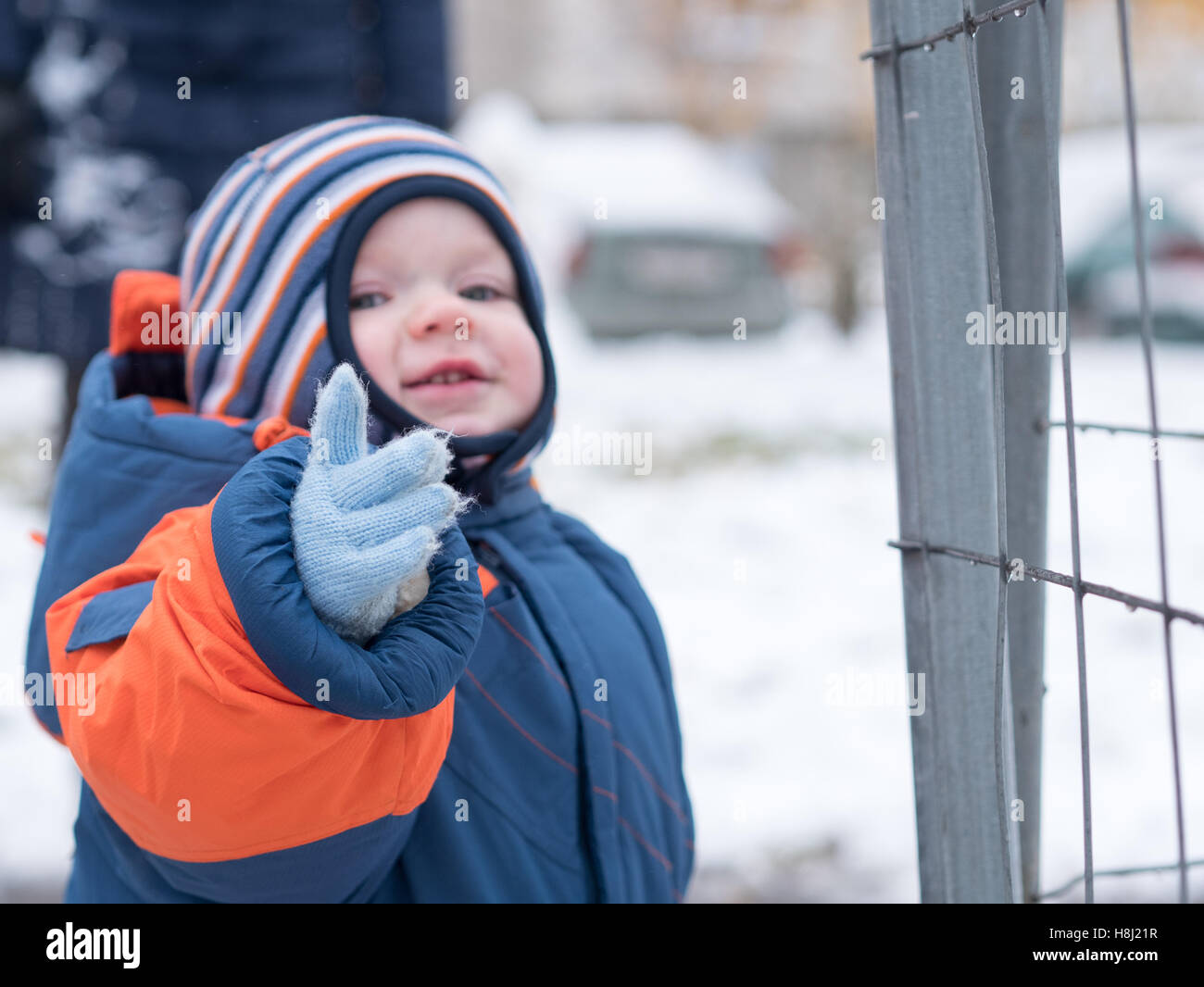 Attraente baby boy giocando con la prima neve. Egli sorride e guarda pupazzo di neve. Spessa blu-tuta arancione a strisce luminose hat su un anno-vecchio figlio. Foto Stock