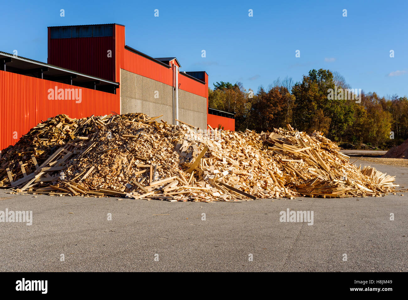 Pila di detriti di legno nella parte anteriore del rosso edificio industriale. Il legno è uno scarto dalla segheria e sarà realizzato in trucioli di legno una Foto Stock