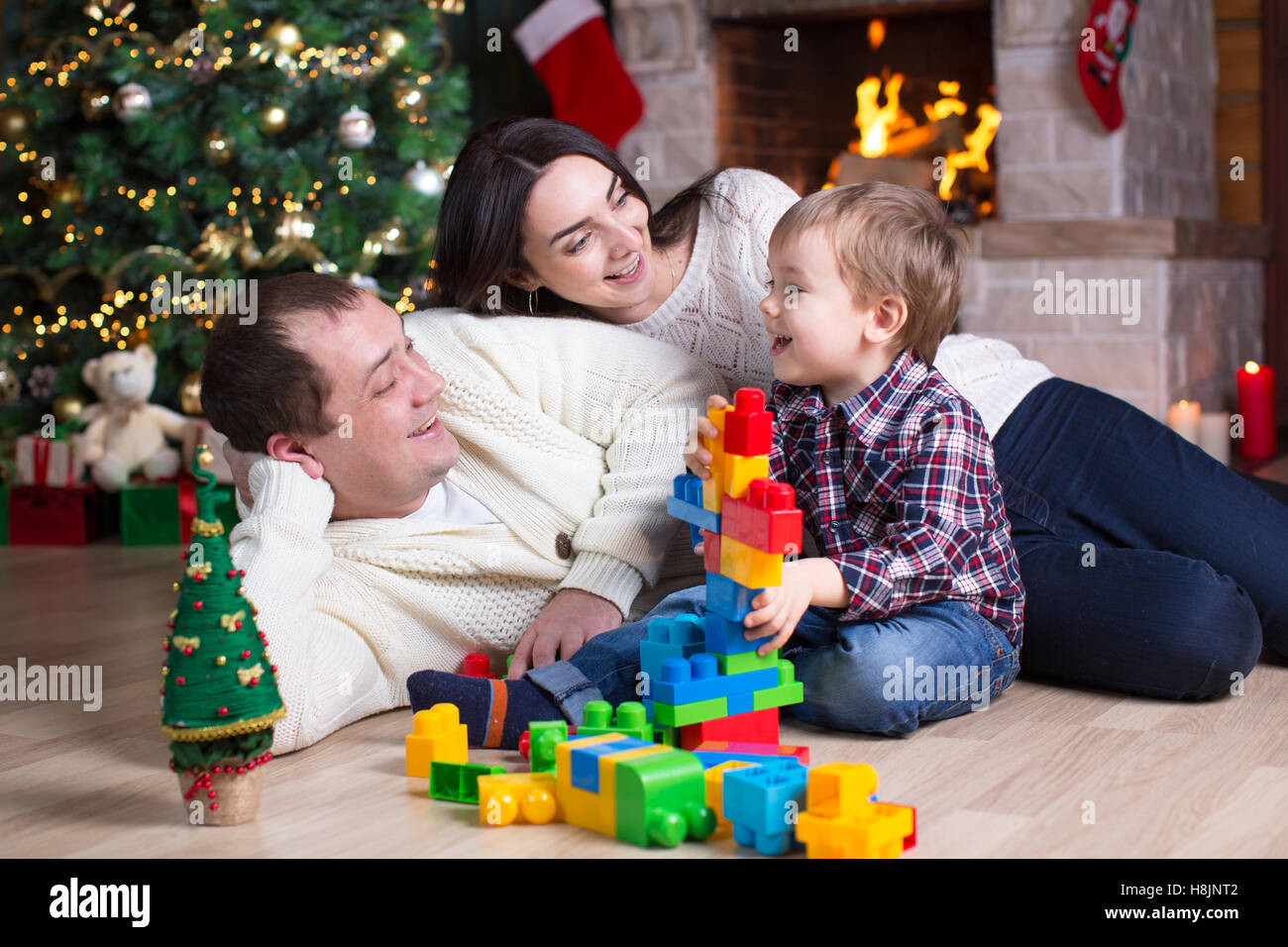 Ragazzo del bambino e i suoi genitori a giocare con i giocattoli di blocco sotto l'albero di natale Foto Stock