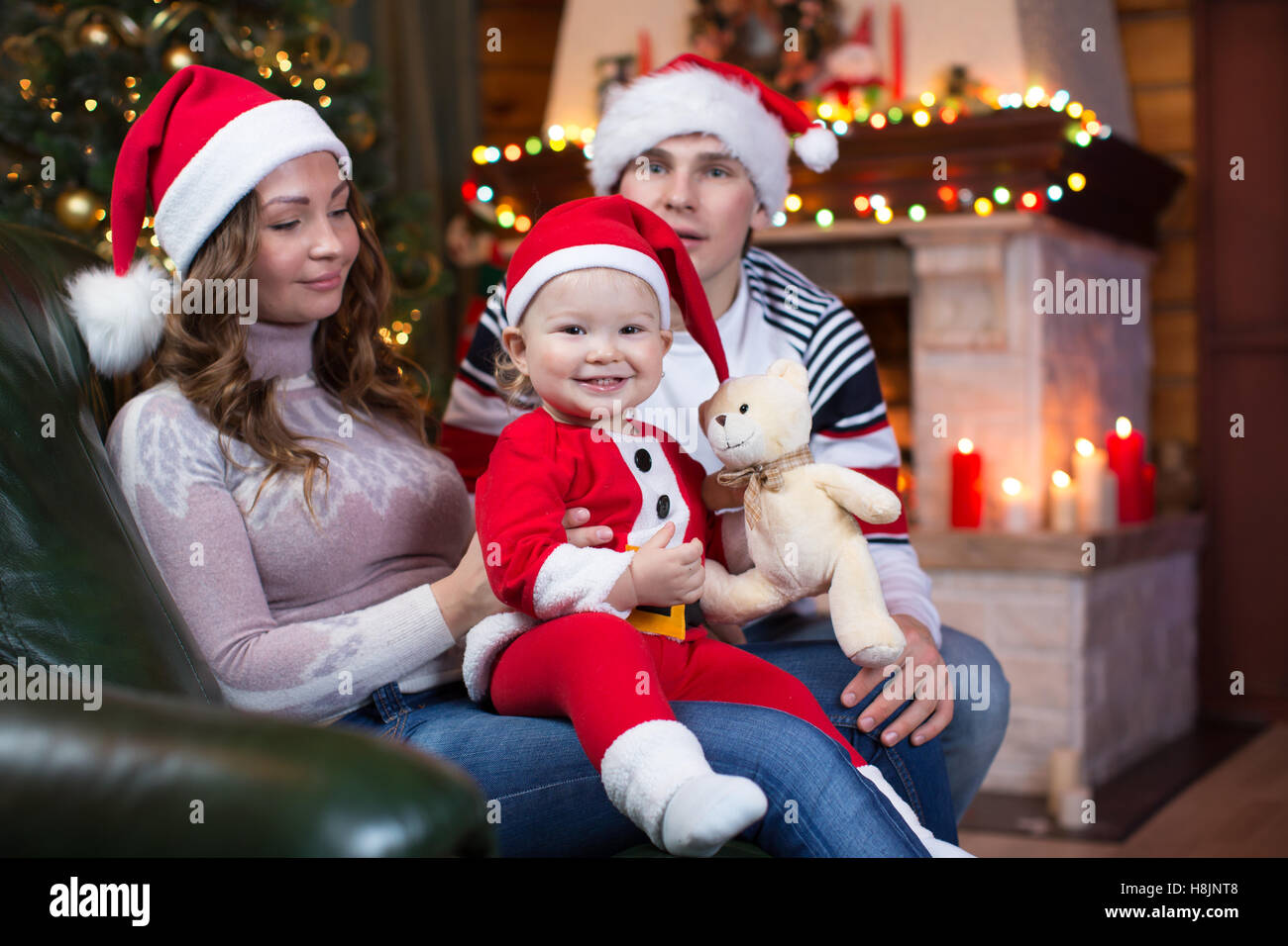 Padre, madre e bambino in santa abito rosso sorriso su uno sfondo di alberi di Natale all'interno della casa Foto Stock