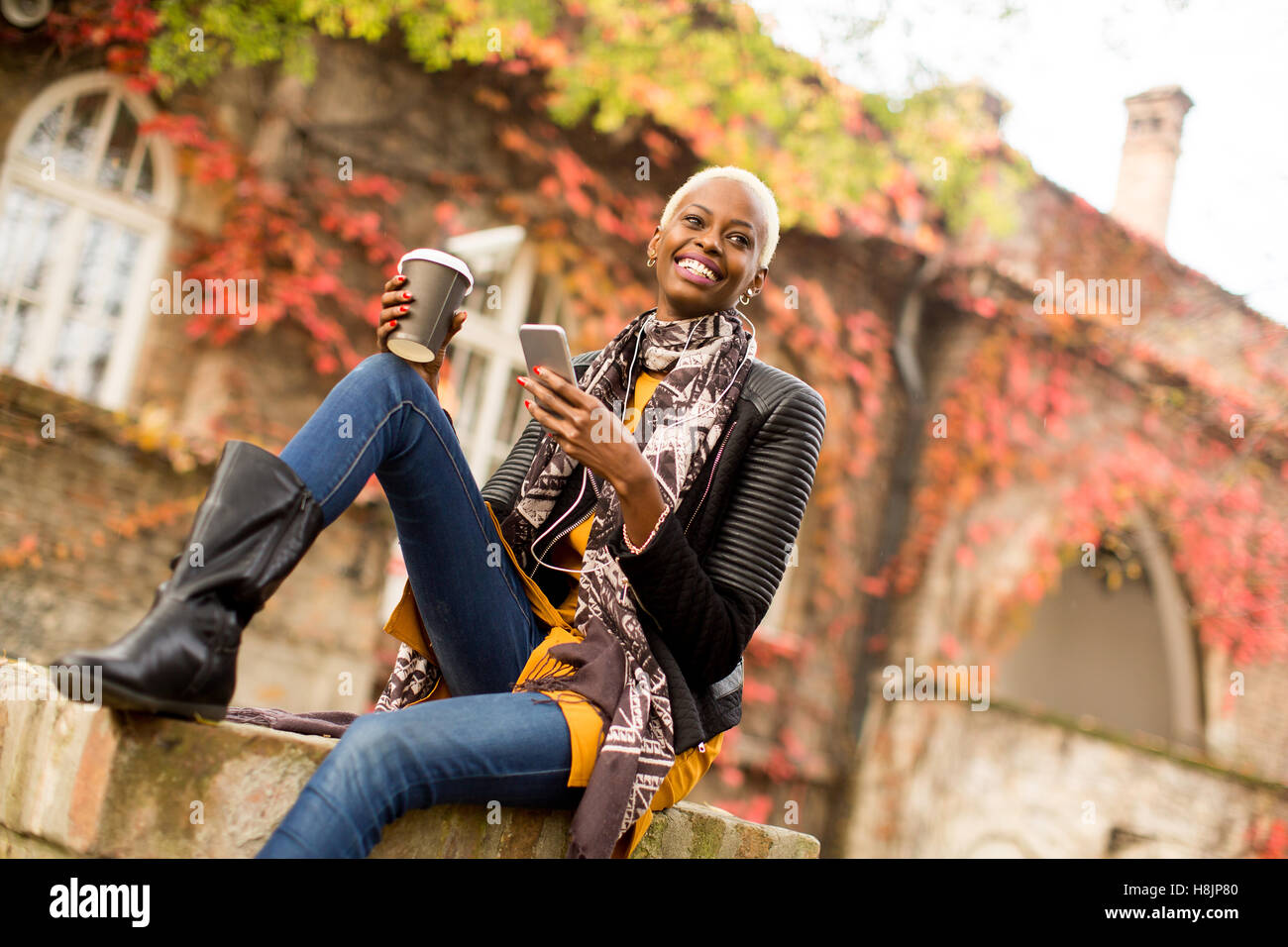 Moderno e giovane africano donna americana in posa con caffè di andare e il telefono cellulare all'aperto Foto Stock