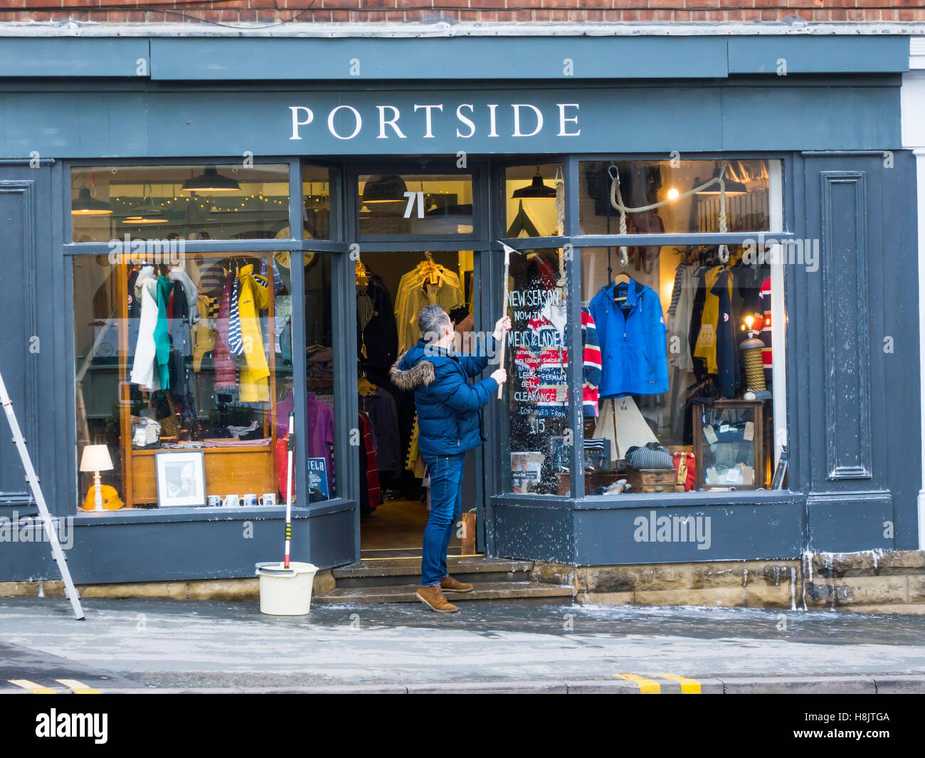 Uomo con mops e acqua insaponata la pulizia di vetri e di vernice sulla parte anteriore del 'Portside' un negozio di abbigliamento a Whitby Noeth Yorkshir Foto Stock