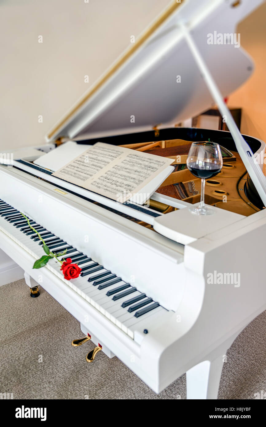 Una rosa rossa sul pianoforte con foglio di musica e un bicchiere di vino rosso Foto Stock