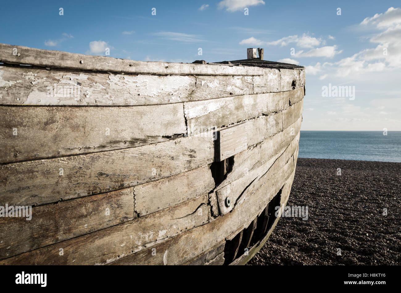 Scafo di un vecchio decadendo a remi in legno barca da pesca con fori su una spiaggia di ciottoli in riva al mare Foto Stock
