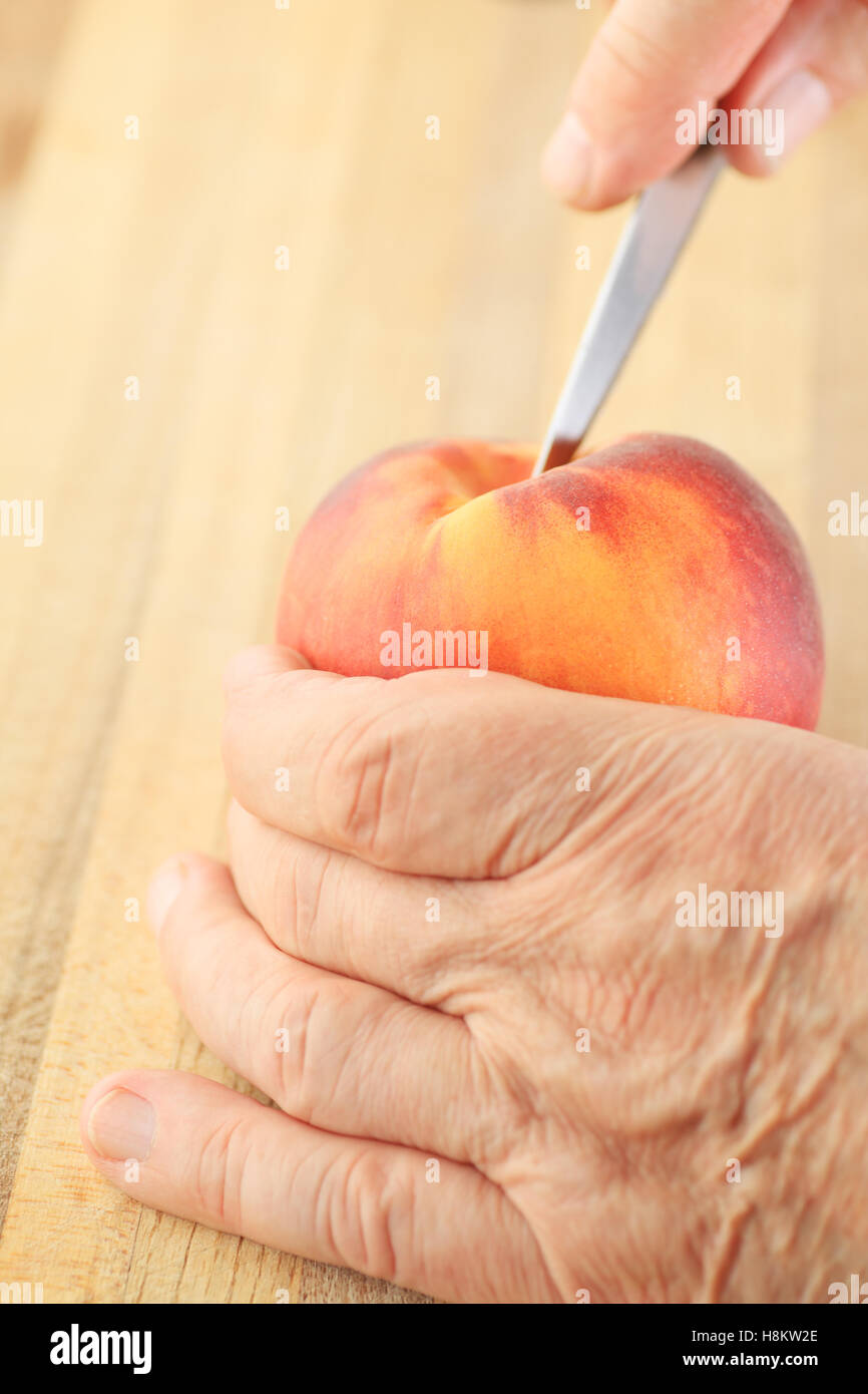Un uomo taglia in una pesca con un coltello seghettato. Foto Stock