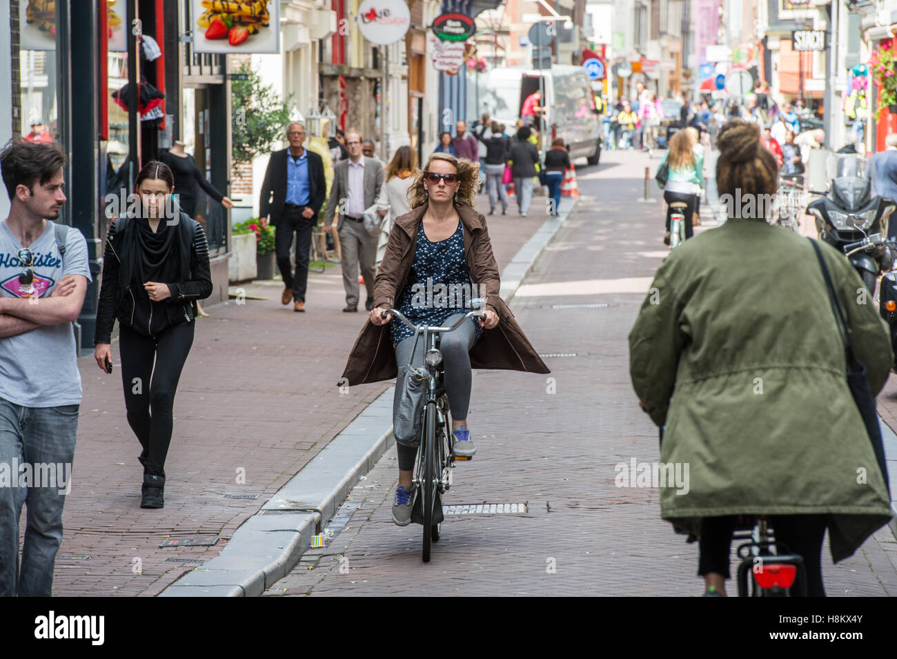 Amsterdam, Paesi Bassi la gente a piedi e in bici equitazione attraverso una trafficata strada laterale con negozi e ristoranti locali. Foto Stock