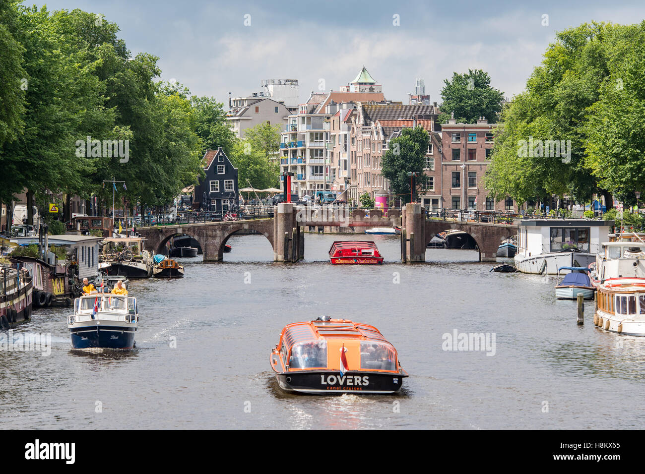 Amsterdam, Paesi Bassi waterfront vista delle barche a vela attraverso un canale di Amsterdam. In fondo è un ponte storico e Foto Stock