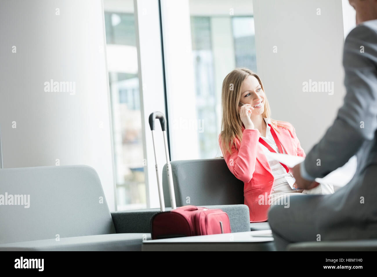 Sorridente imprenditrice utilizzando smart phone mentre è seduto alla lobby e nel centro congressi Foto Stock
