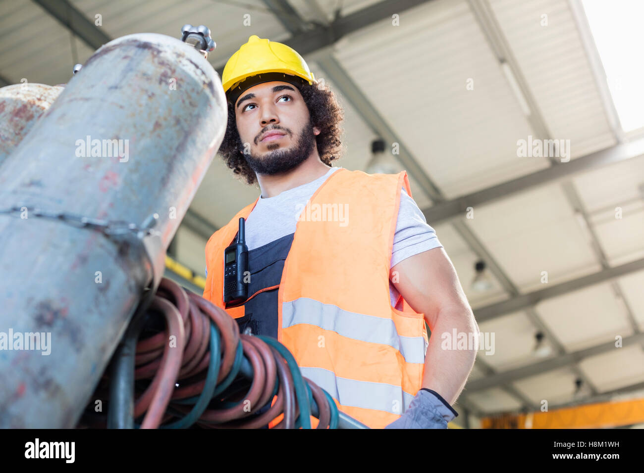 Basso angolo vista del giovane lavoratore manuale muovendo la bombola di gas nel settore metalmeccanico Foto Stock