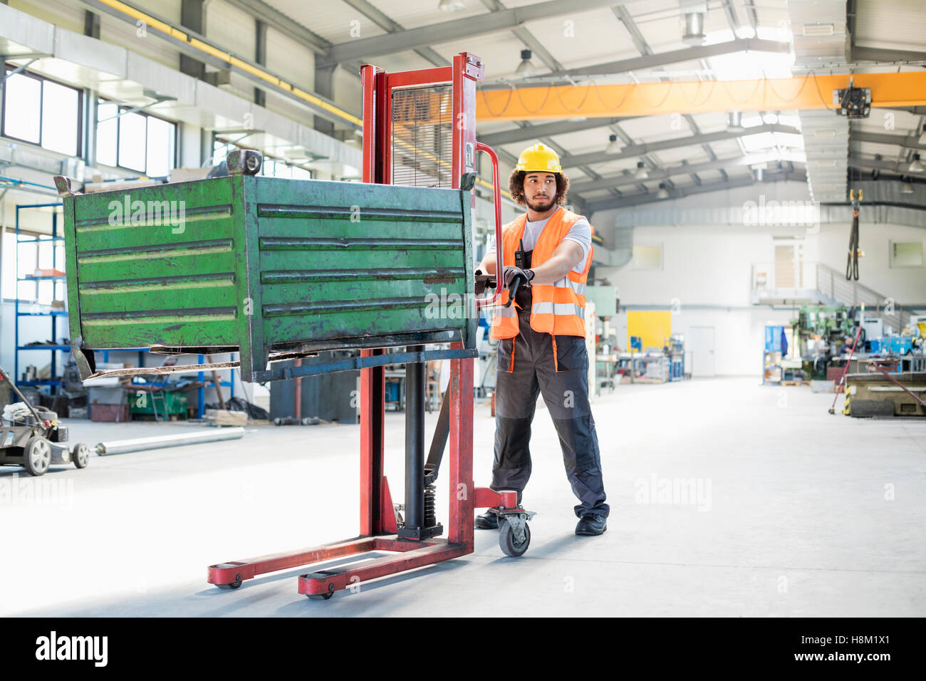 Per tutta la lunghezza della giovane lavoratore manuale spingendo il carrello a mano con metalli pesanti nell'industria Foto Stock