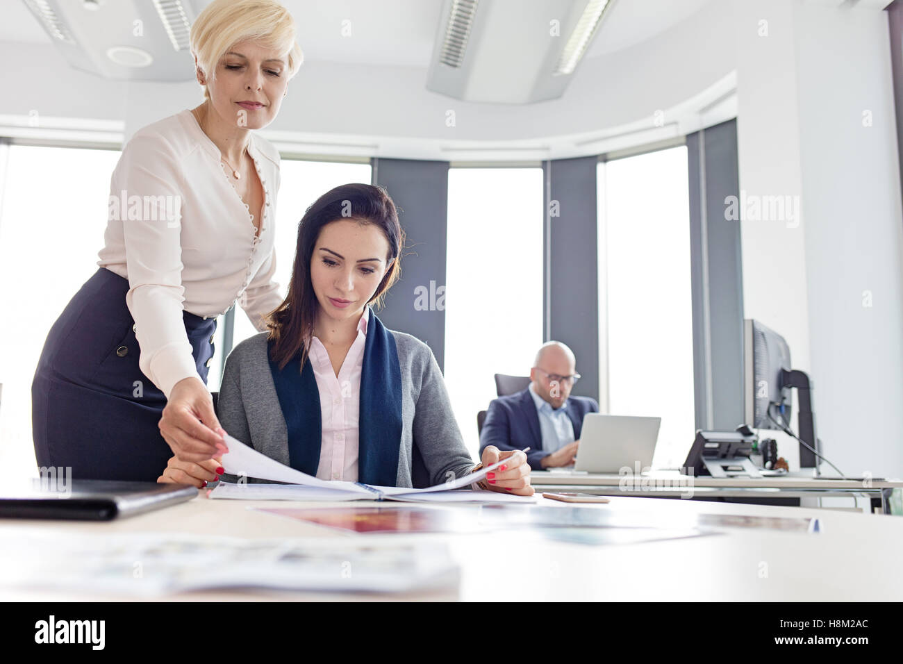 Imprenditrici libro di lettura con il collega di sesso maschile in background in ufficio Foto Stock