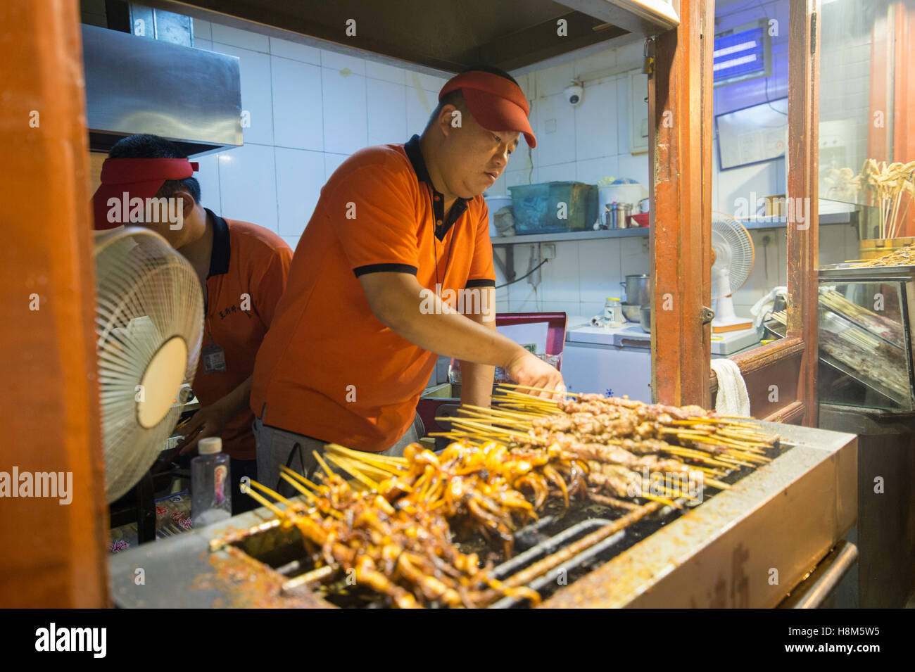 Pechino, Cina - Chef la cottura della carne su bastoni in la Donghuamen Snack Mercato Notturno, un grande mercato all'aperto che è un attrazione Foto Stock