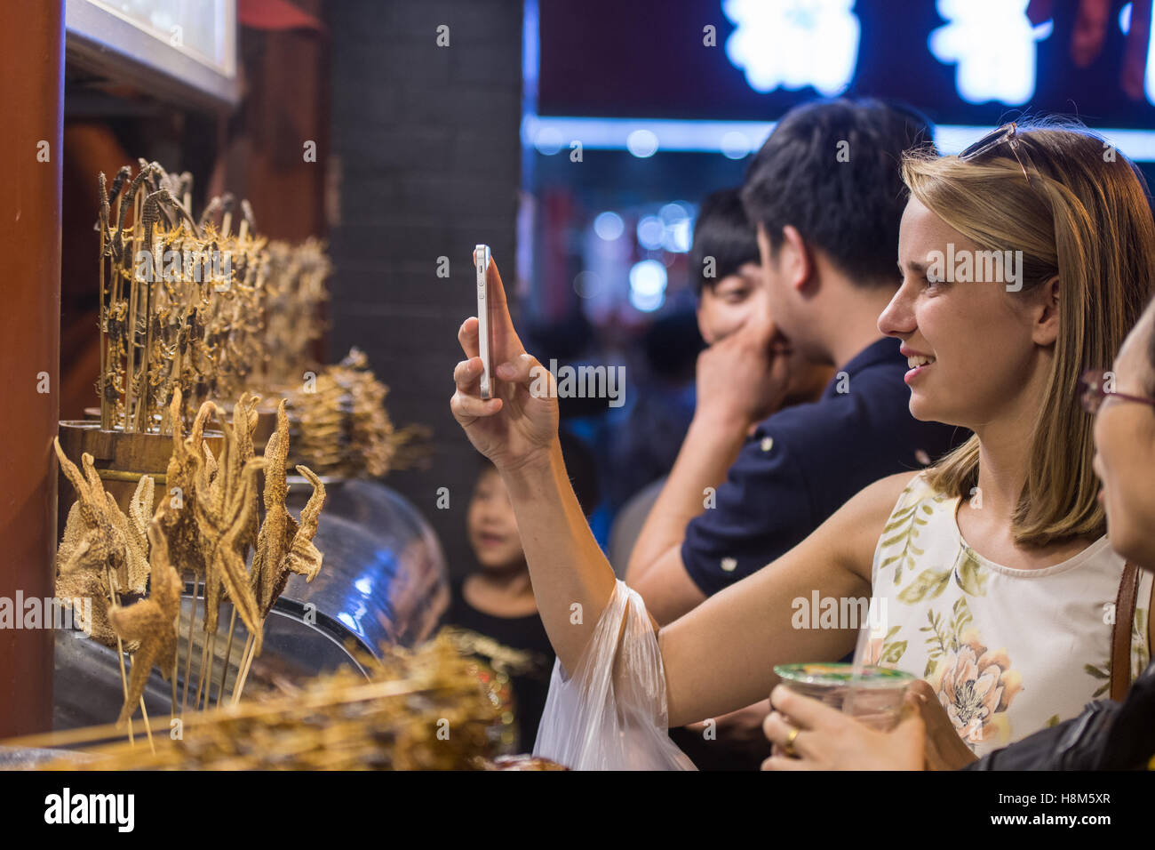 Pechino, Cina - turista femminile di scattare una foto sul suo telefono cellulare di scorpioni e starfish su bastoni in vendita presso la Donghuame Foto Stock