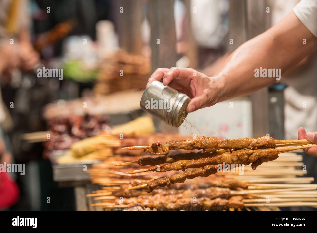 Pechino, Cina - cuocere scuotendo le spezie sopra la carne su un bastone per la vendita presso la Donghuamen Snack Mercato Notturno, un grande mercato all'aperto Foto Stock