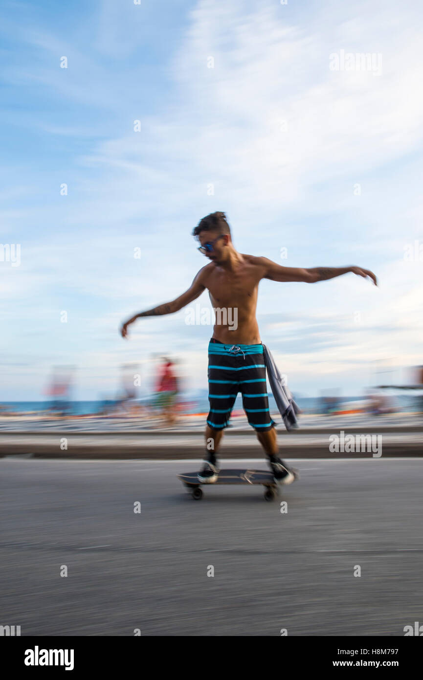 RIO DE JANEIRO - Marzo 6, 2016: Giovani carioca brasiliano sulla skateboard si muove in una sfocatura di movimento lungo la spiaggia di Ipanema. Foto Stock