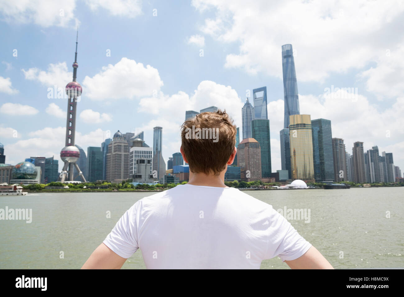 Vista posteriore di un uomo guarda lo skyline di Pudong contro il cielo nuvoloso Foto Stock