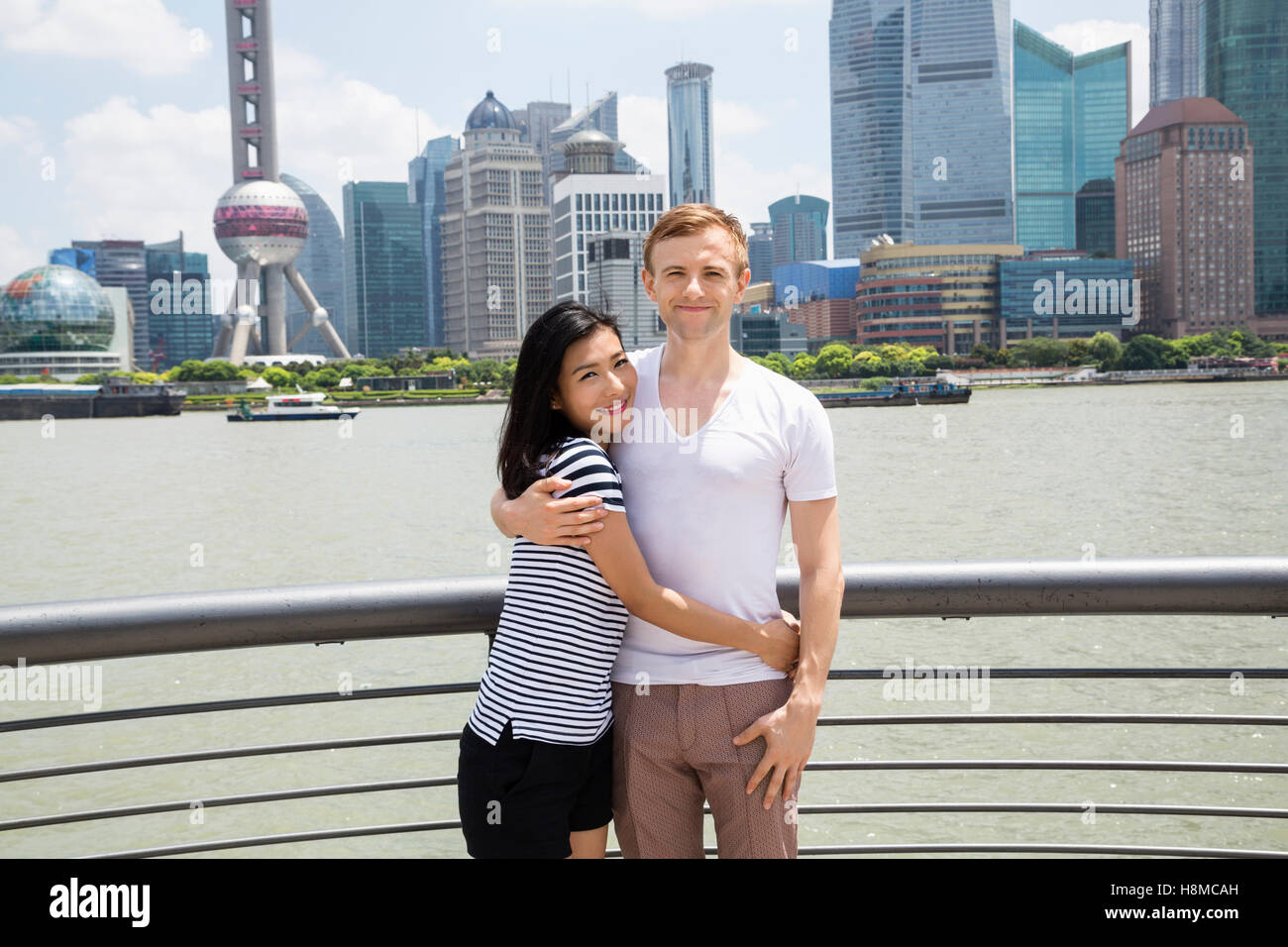 Ritratto di Coppia sorridente in piedi dalla ringhiera con lo skyline di Shanghai in background Foto Stock