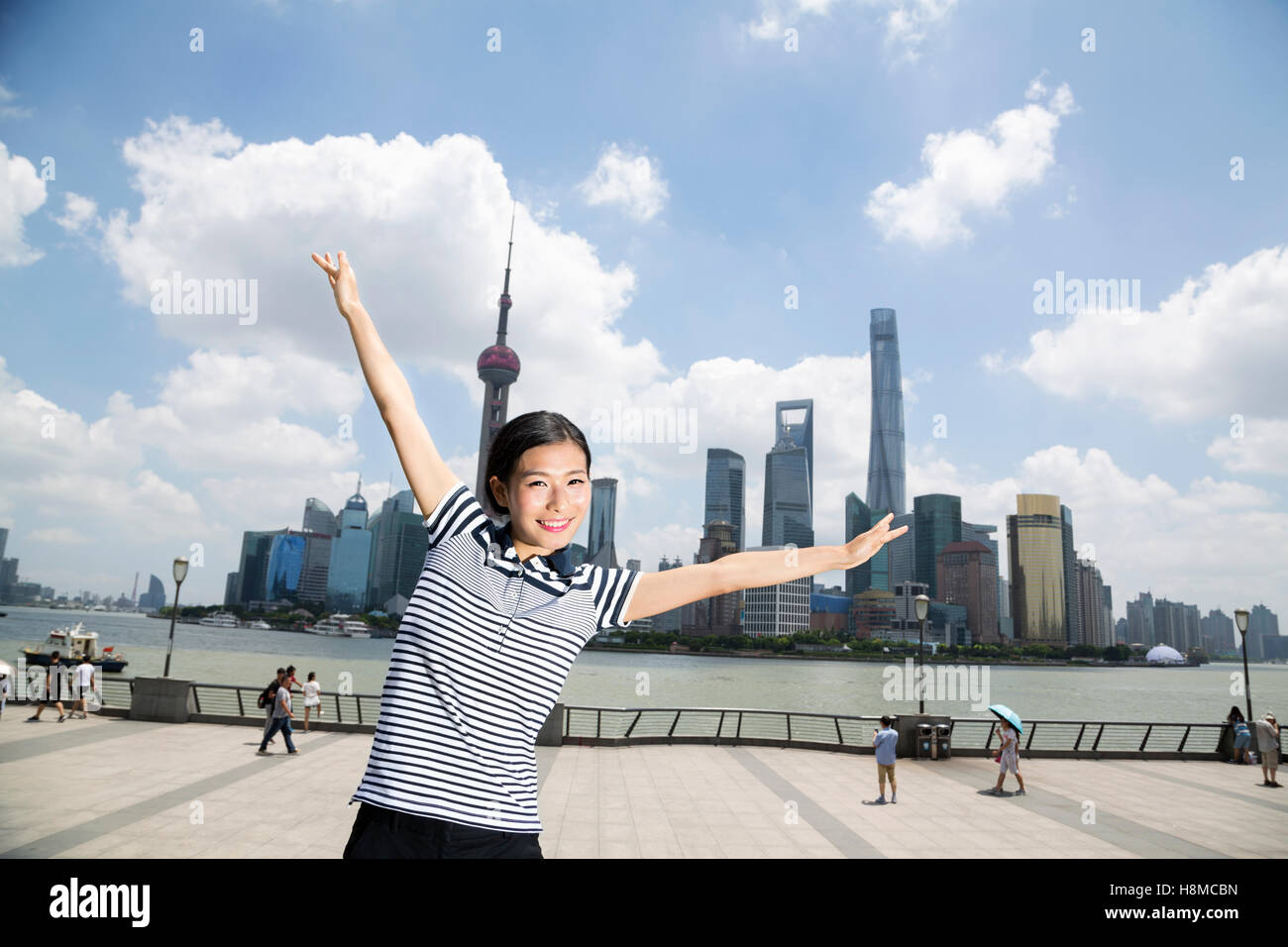 Ritratto di donna felice in piedi con le braccia distese sul lungomare contro lo skyline di Pudong Foto Stock
