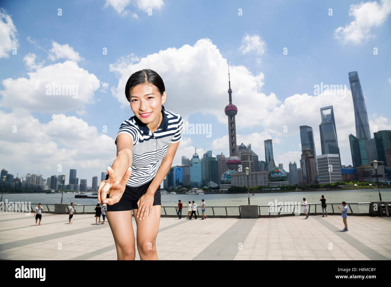 Ritratto di donna felice gesti segno di pace mentre si sta in piedi sul lungomare contro lo skyline di Pudong Foto Stock