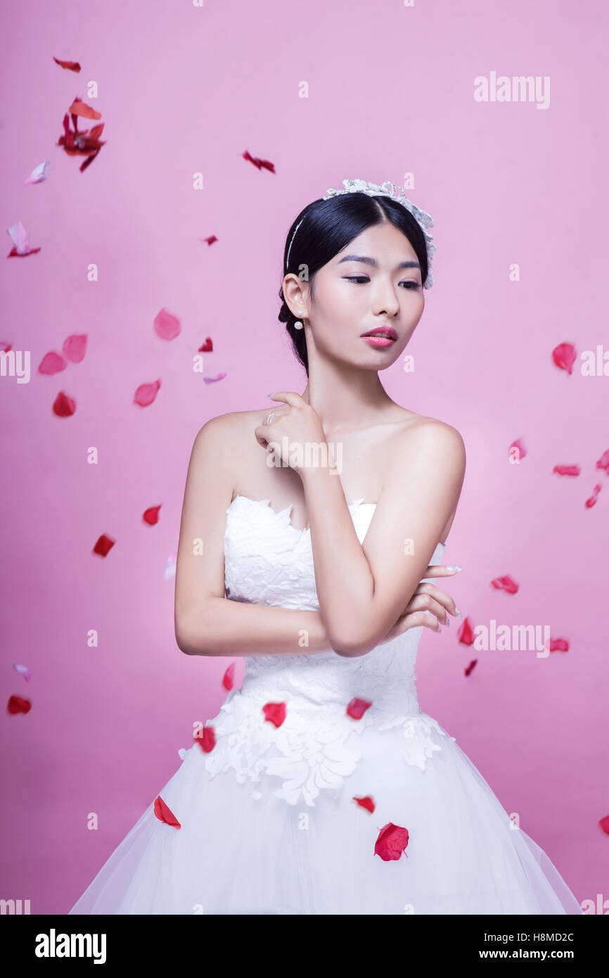 Bella Sposa con petali di rosa a mezz aria in piedi contro sfondo rosa Foto Stock