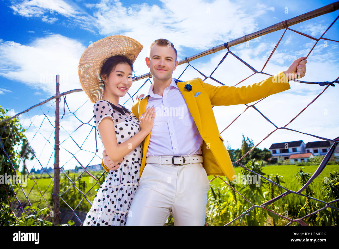 Ritratto di coppia felice in piedi da recinzione al campo contro sky Foto Stock