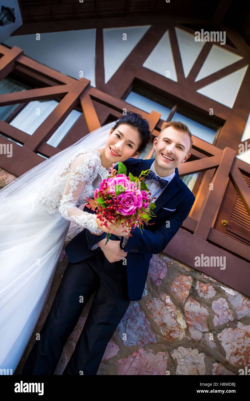 Angolo basso ritratto di felice matrimonio giovane azienda bouquet di fiori contro la casa Foto Stock