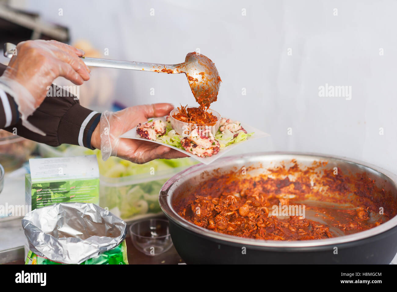 Cucina di strada. Le mani del cuoco preparare un piatto di seppie in umido. Foto Stock