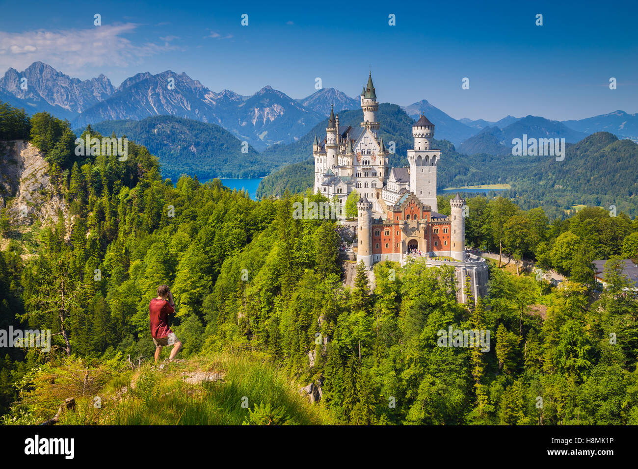 Visualizzazione classica del famoso castello di Neuschwanstein con maschio tourist godendo della splendida vista da una ripida scogliera, Füssen Baviera, Germania Foto Stock