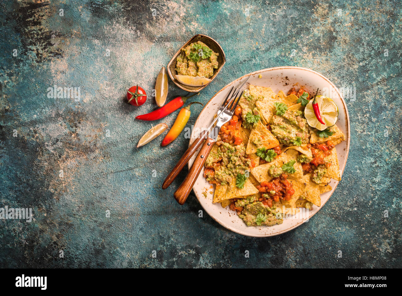 Mais giallo nacho chips farcite con carne di manzo macinata, guacamole, formaggio fuso, peperoni e foglie di prezzemolo nella piastra sulla pietra blu Foto Stock
