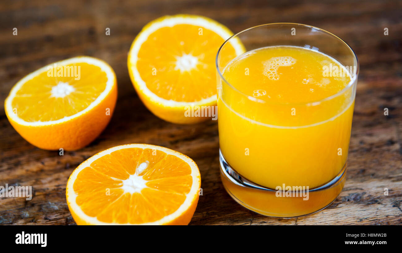 Bicchiere di succo di frutta fresco e tagliare le arance sul tavolo di legno Foto Stock