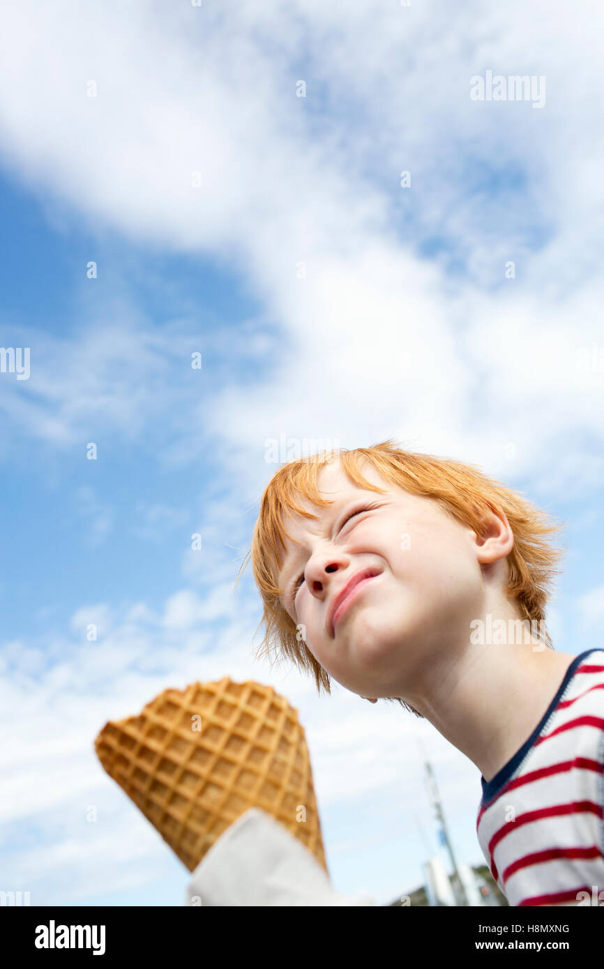 Basso angolo di vista redhead ragazzo (6-7) a mangiare il gelato contro sky Foto Stock