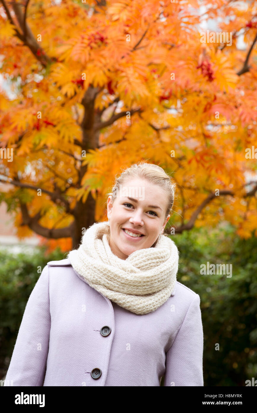 Giovane donna indossa soprabito contro autumn tree Foto Stock
