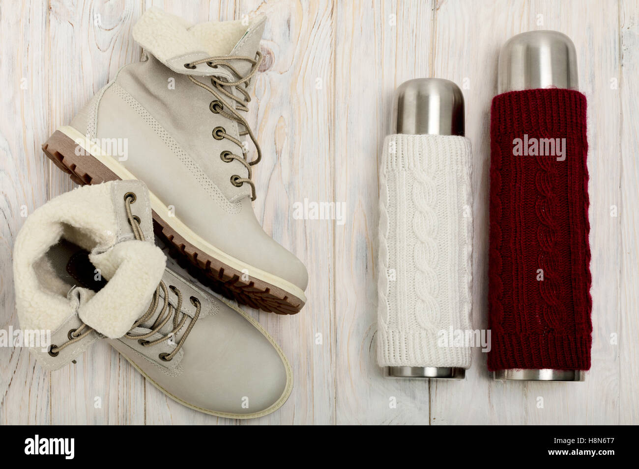 Luce invernale stivali e un thermos in la maglia del coperchio sul luminoso sullo sfondo di legno. Foto Stock