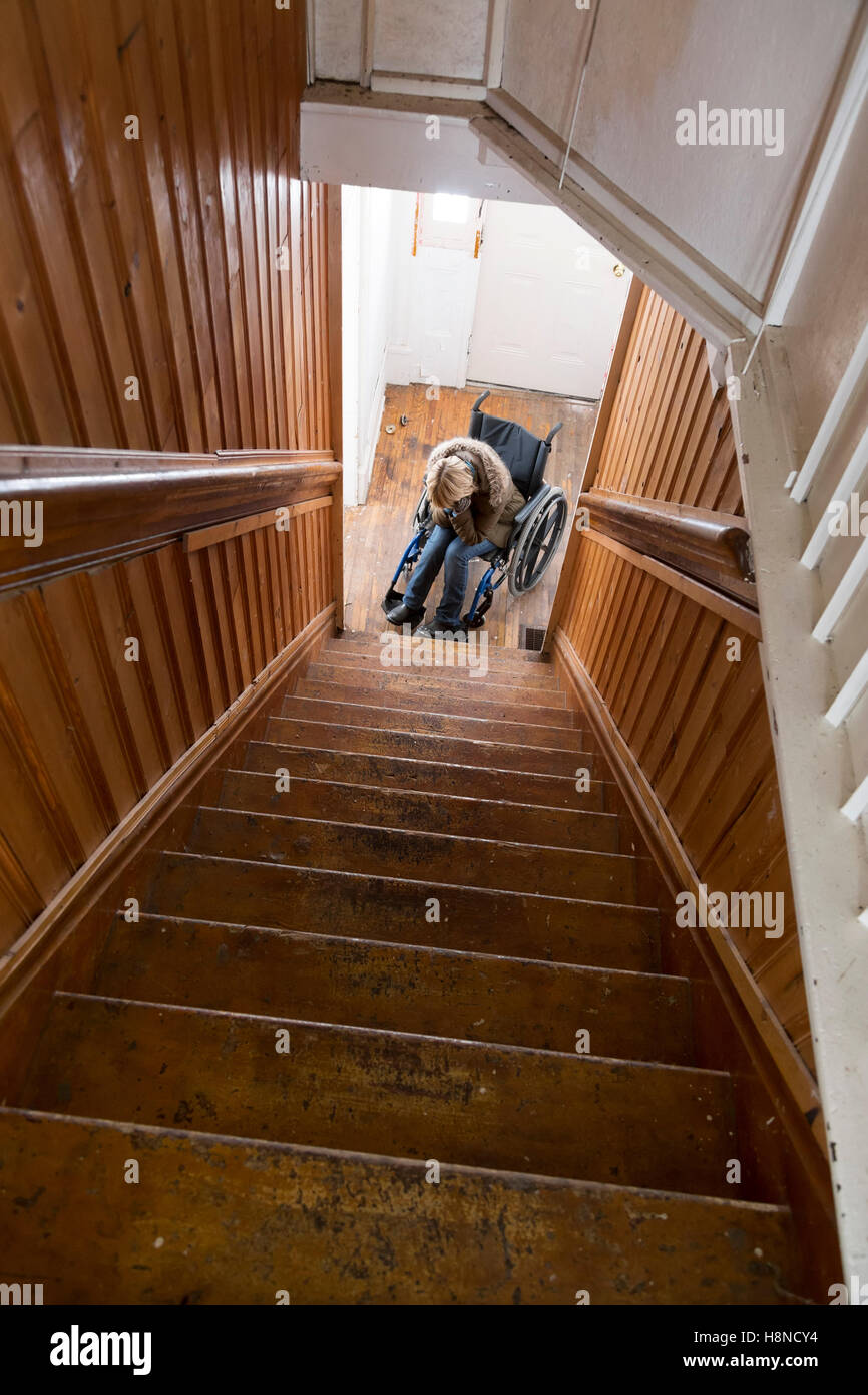 Giovane donna in sedia a rotelle al fondo delle scale Foto Stock