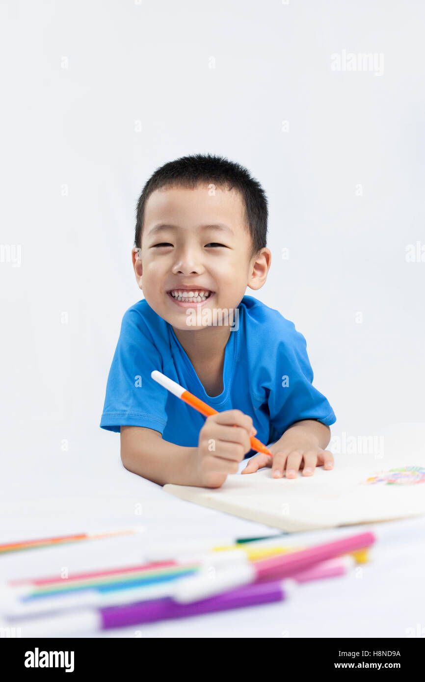 Happy Little Chinese Boy colorazione mentre sdraiato sul pavimento Foto Stock