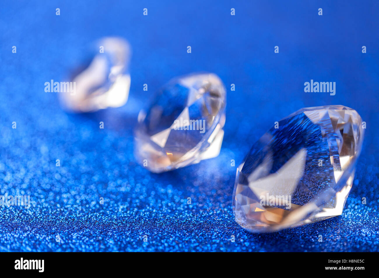 Tre grand caro diamanti prevista sulla diagonale su blu scintillante di paillettes sfondo, macro . Grande brillante closeup. Foto Stock
