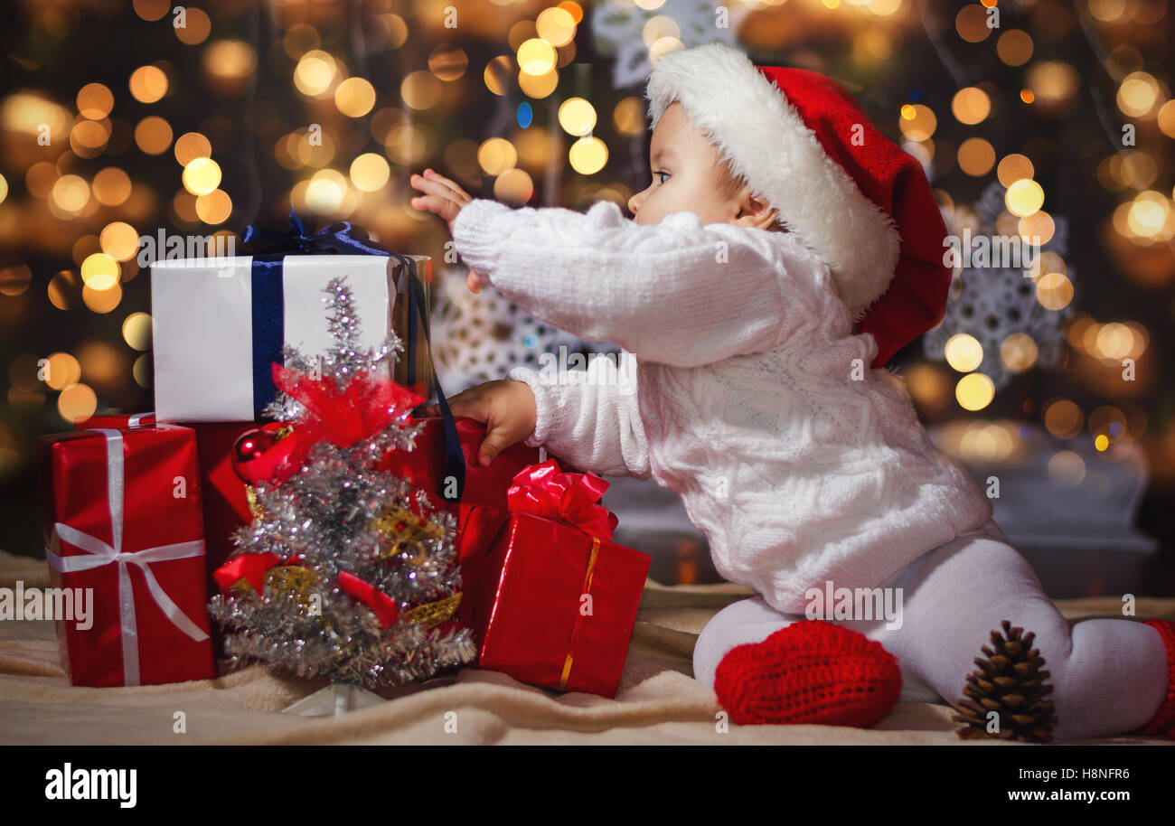 Cerca Natale.Piccolo Bambino Nel Cappello Di Babbo Natale Cerca Di Ottenere Una Mano Per Le Scatole Di Doni Contro Lo Sfondo Di Una Ghirlanda Di Natale Foto Stock Alamy