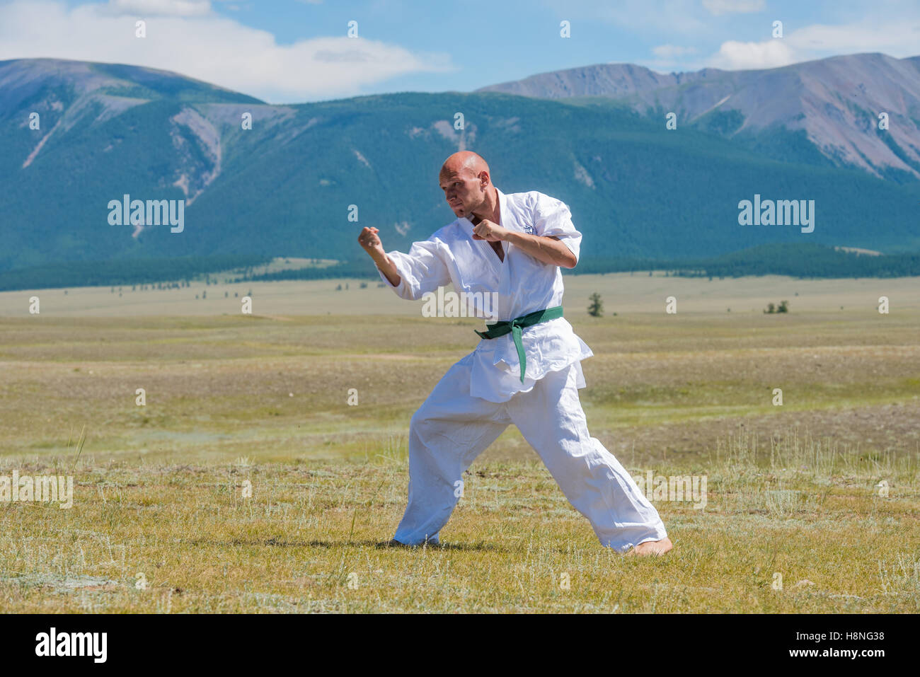 Uomo in bianco kimono e Allenamento cinture nere kung-fu, karate o aikido su sfondo di montagna. Foto Stock