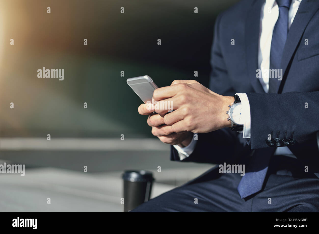 Ritaglia maschio senza volto in abito nero di contenimento e utilizzando il telefono al di fuori seduta sul parapetto Foto Stock
