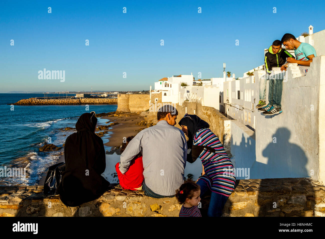Popolo marocchino si affacciano sulle mura di cinta Medina di Asilah al tramonto, Asilah, Marocco Foto Stock
