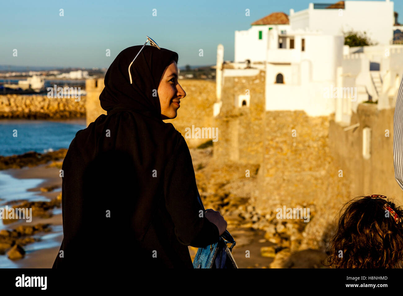 Una giovane donna marocchina si affaccia sulla città murata di Asilah al tramonto, Marocco Foto Stock